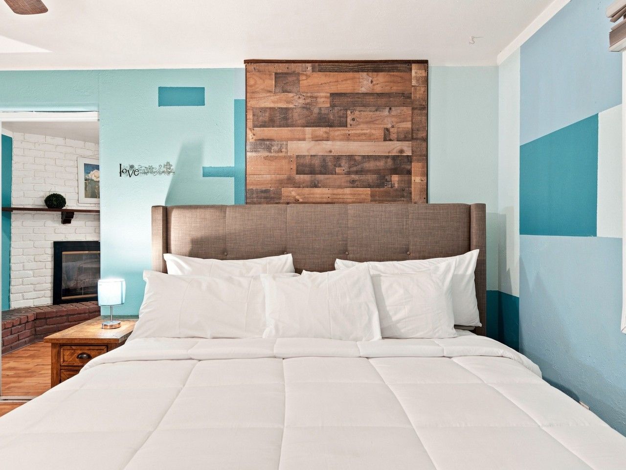 A hotel room with a large bed, a wooden headboard, a fireplace, and a wall with a blue and white color scheme.