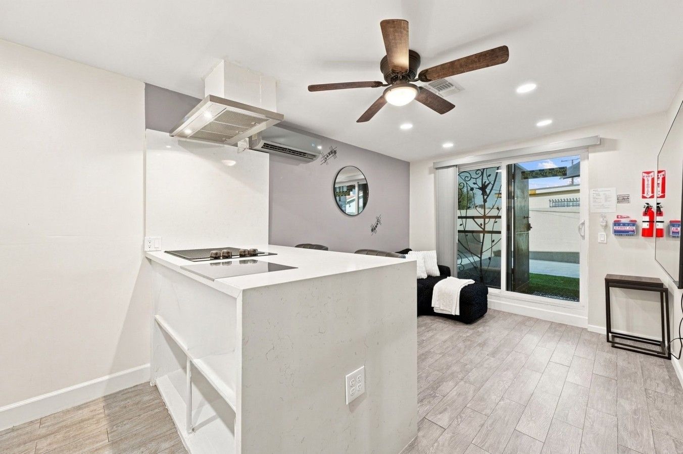 Une cuisine moderne dotée d’un îlot central, d’un ventilateur de plafond et offrant une vue sur l’extérieur grâce à une porte vitrée.