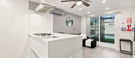 A modern kitchen with a central island, a ceiling fan, and a view of the outside through a glass door.