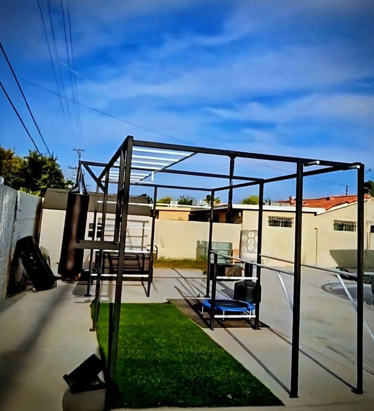A metal structure with a roof, possibly a gym or play area, in a backyard with a green lawn and a white wall.