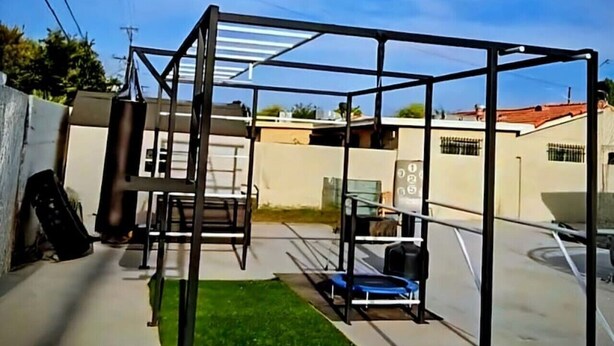Estructura metálica con techo, posiblemente un gimnasio o área de juegos, en un entorno exterior con cielo despejado.