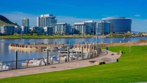Un puerto deportivo con barcos amarrados, un paseo marítimo y edificios modernos al fondo.