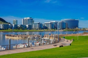 A marina with boats docked, a waterfront promenade, and modern buildings in the background. - Your stay, your way, with pool, gym & CalKing Bed. (Phoenix)