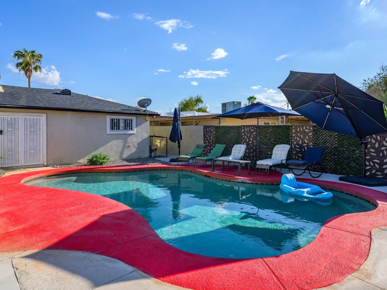 A swimming pool with a red border, surrounded by lounge chairs and umbrellas.