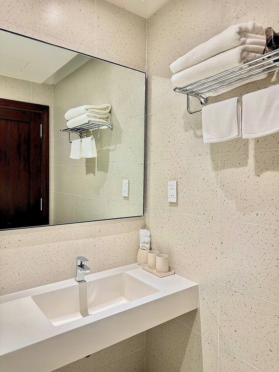 Un baño con lavamanos, espejo, toallero y puerta de madera.