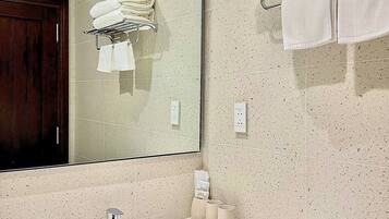 Un baño con lavamanos, espejo, toallero y puerta de madera.