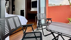 Una habitación de hotel compacta con balcón, cama, televisión y un pequeño rincón de descanso.
