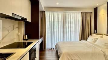 Una habitación de hotel moderna con cocina, una cama y un ventanal con cortinas.
