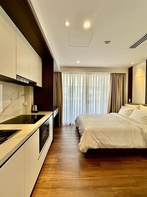 Une chambre d’hôtel moderne dotée d’un coin cuisine, d’un lit et d’une grande fenêtre avec des rideaux.