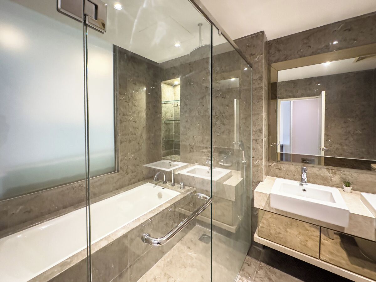 A modern bathroom with a glass shower enclosure, a bathtub, and two sinks with a marble countertop.