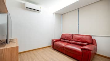 Una habitación con un sofá de cuero rojo, un televisor de pantalla plana sobre un soporte de madera y un equipo de aire acondicionado instalado en la pared.