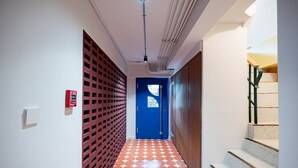 A hallway with a red lattice partition, a blue door, and a staircase with a wooden handrail. - Charoen One (Bangkok)