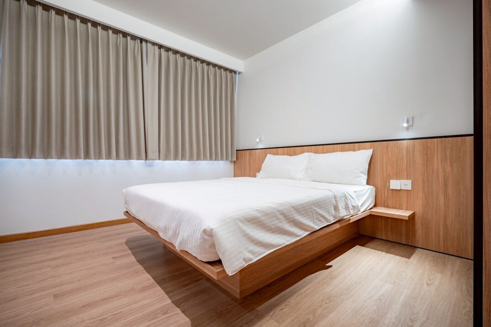 A modern bedroom with a wooden bed frame, a bedside table, and a window with curtains.