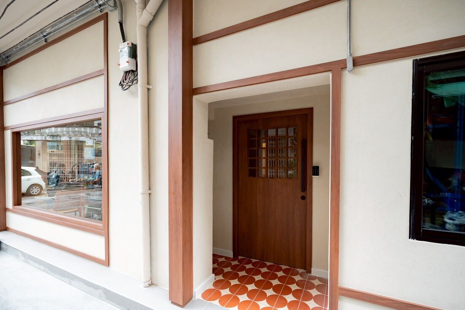 A building entrance with a wooden door, a window with a view of the street, and a tiled floor.