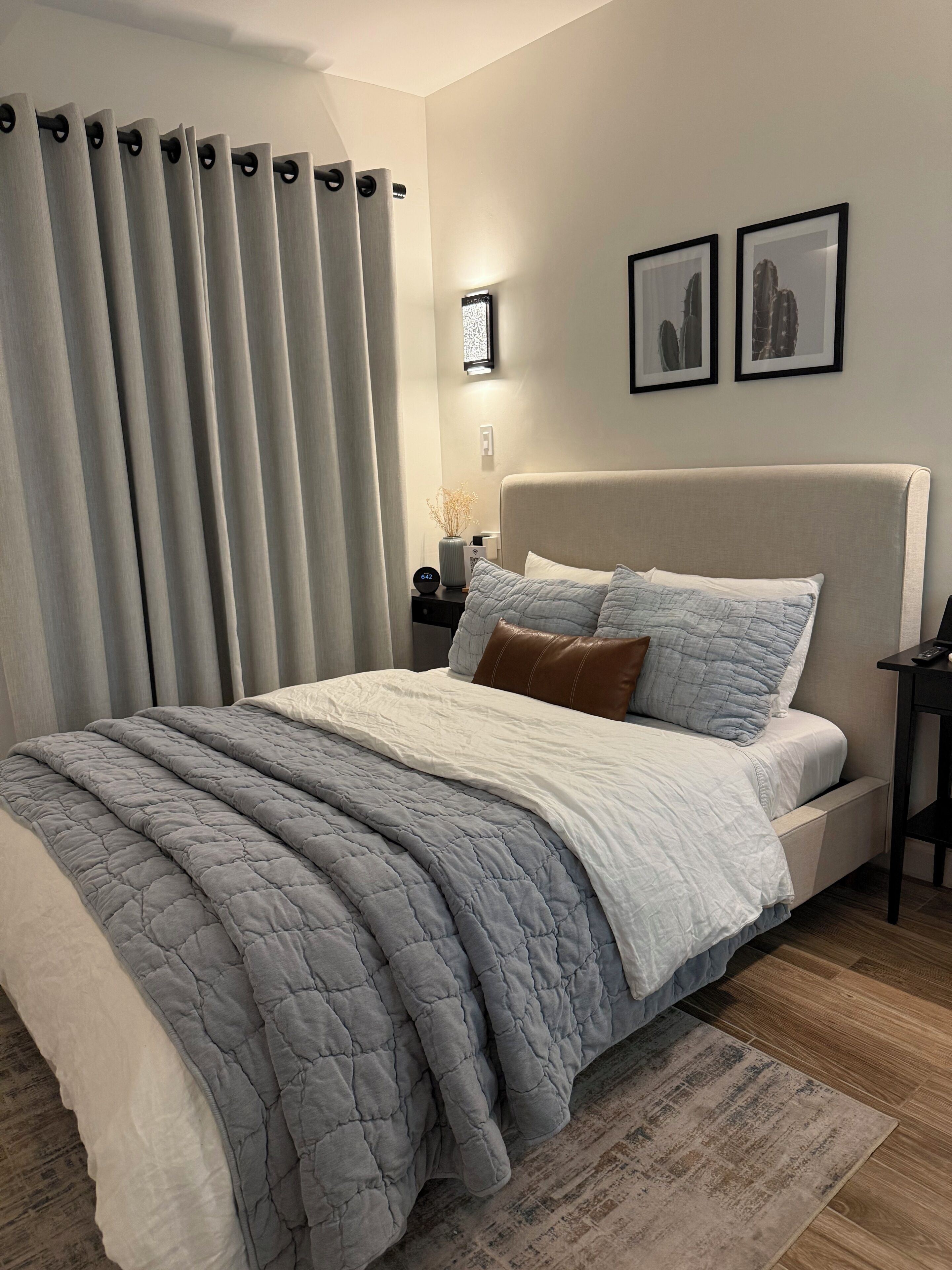 A bedroom with a bed, curtains, a nightstand, a lamp, and framed pictures on the wall.