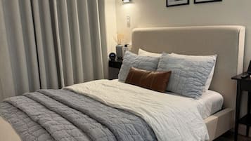 A bedroom with a bed, curtains, a nightstand, a lamp, and framed pictures on the wall.