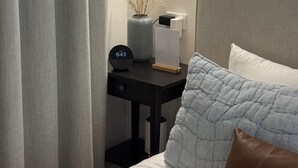A neatly made bed with a pillow, a bedside table with a clock and a vase, and a wall-mounted light. - Casa Oasis Boutique (Hermosillo)