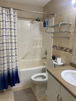 Ein Badezimmer mit Badewanne, Toilette und Waschbecken. Vorhanden sind ein Duschvorhang, ein Handtuchhalter und ein Blumentopf.