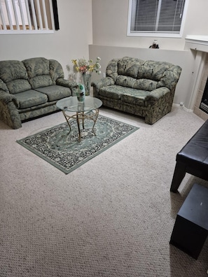 Ein Wohnzimmer mit zwei getarnten Sofas, einem Glastisch und einem gemusterten Teppich.