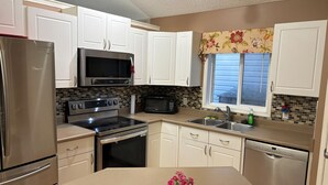 A kitchen with white cabinets, stainless steel appliances, a microwave, stove, oven, dishwasher, and a window with floral curtains. - 
Holiday Home in West Edmonton (Edmonton)