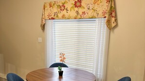 A dining area with a round wooden table, four dark blue chairs, a potted plant, and a window with blinds and a floral valance. - 
Holiday Home in West Edmonton (Edmonton)