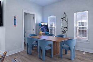 Ein Zimmer mit einem Holztisch, vier blauen Stühlen, einer Spielmaschine und einer Surfbrett-Dekoration.
