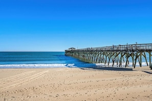 Ein Strand mit einer hölzernen Seebrücke, die sich ins Meer erstreckt.