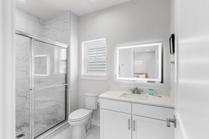 A modern bathroom with a glass shower enclosure, a toilet, a sink with a mirror above it, and a cabinet below. - Hang Ten House 2.5 Blocks to Beach Pet Friendly (Myrtle Beach)