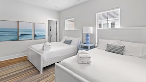A hotel room with two beds, a ceiling fan, a window with blinds, a nightstand with a lamp, and a wall with framed artwork. - Hang Ten House- 2.5 Blocks to Beach- Pet Friendly (Myrtle Beach)