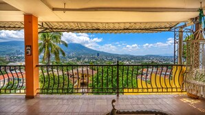 A balcony with a view of a cityscape, a palm tree, and a mountain in the distance. - Skyline & Volcano San Salvador (SAN SALVADOR)