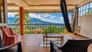 A balcony with a view of a cityscape and a mountain, furnished with chairs and a table.