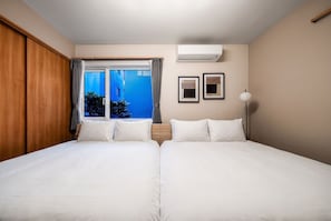 A hotel room with a large bed, a window with curtains, a wall-mounted air conditioner, and two framed pictures. - THE AVELIA (Saporo)