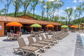 A poolside area with lounge chairs and umbrellas, wooden cabins, and a clear sky. - Resort Cabin > Golf Cart! > Hot Tub > Lazy River > Indoor Pool > Shuffleboard (Hollister)