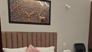 Een net opgemaakt bed met een witte dekbedovertrek en een roze kussen, een ingelijst kunstwerk erboven, en een donker vloerkleed.