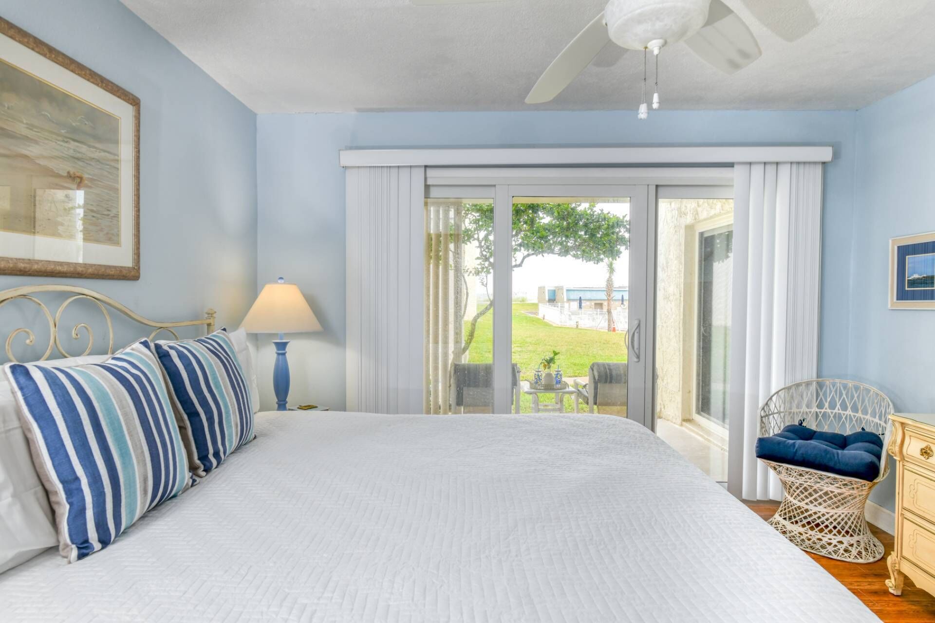 A bedroom with a bed, a nightstand, a lamp, a chair, and a view of the outdoors.