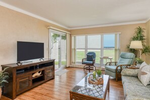 Ein Wohnzimmer mit Flachbildfernseher, einer Holzunterhaltungsecke, einem Glastisch und Korbstühlen sowie einer Couch.