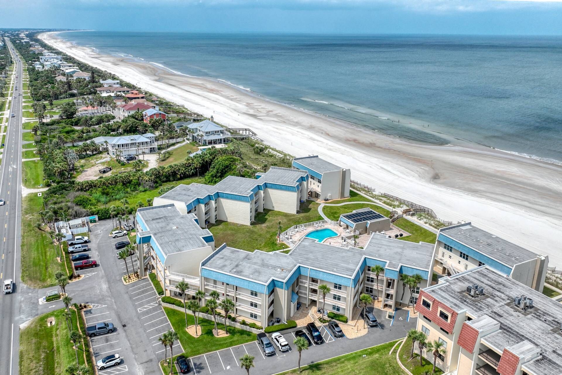 A coastal hotel with a swimming pool, parking, and a view of the beach.