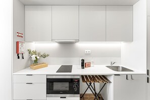 A modern kitchen with white cabinets, a built-in oven, a sink, and a wooden drying rack. - GuestReady - Studio AR (São Mamede de Infesta)