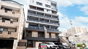 Un edificio residencial de varios pisos con balcones, acceso a un garaje y vehículos estacionados.