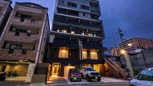 Un edificio residencial de varios pisos con acceso a garaje, vehículos estacionados y una escalera que lleva a los pisos superiores.