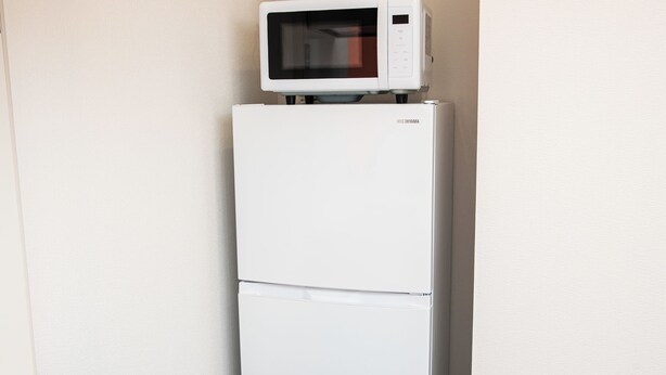 Un refrigerador blanco con un microondas encima, ubicado en un rincón de una habitación de paredes lisas.