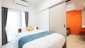 Una habitación de hotel con una cama, una ventana con cortinas, un equipo de aire acondicionado y una puerta corredera que da a una habitación naranja.