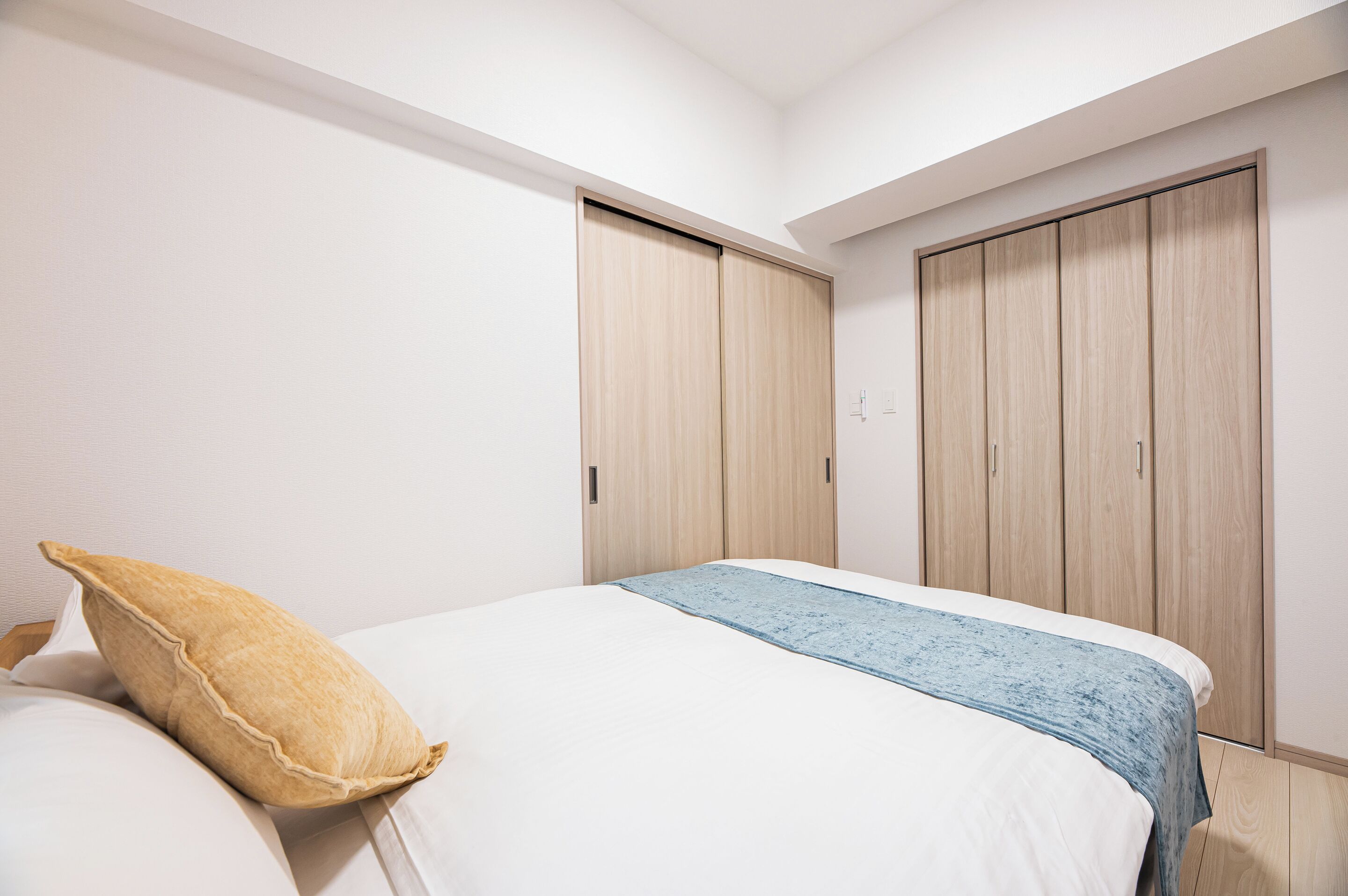 A bedroom with a bed, pillows, a blue blanket, and wooden wardrobes.
