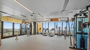 A spacious gym with various exercise equipment, large windows offering a view of the city, and a 'Training Zone' sign. - Live in the clouds! 3BD ultra-luxury in Southbank (Southbank)