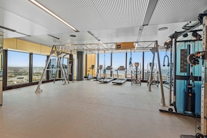 Ein geräumiges Fitnessstudio mit verschiedenen Trainingsgeräten und großen Fenstern mit Blick auf die Stadt, mit einem Schild 'Training Zone'.
