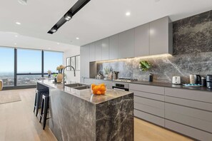A modern kitchen with a marble island, grey cabinetry, and a city view. - Live in the clouds! 3BD ultra-luxury in Southbank (Southbank)