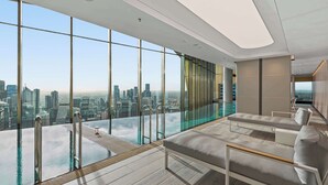 A modern infinity pool with a city view, a lounge area with sofas, and a glass-enclosed section. - Live in the clouds! 3BD ultra-luxury in Southbank (Southbank)