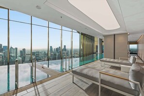 Ein moderner Infinity-Pool mit Stadtblick, eine Lounge-Ecke mit Sofas und ein durchsichtiges, verglastes Becken.