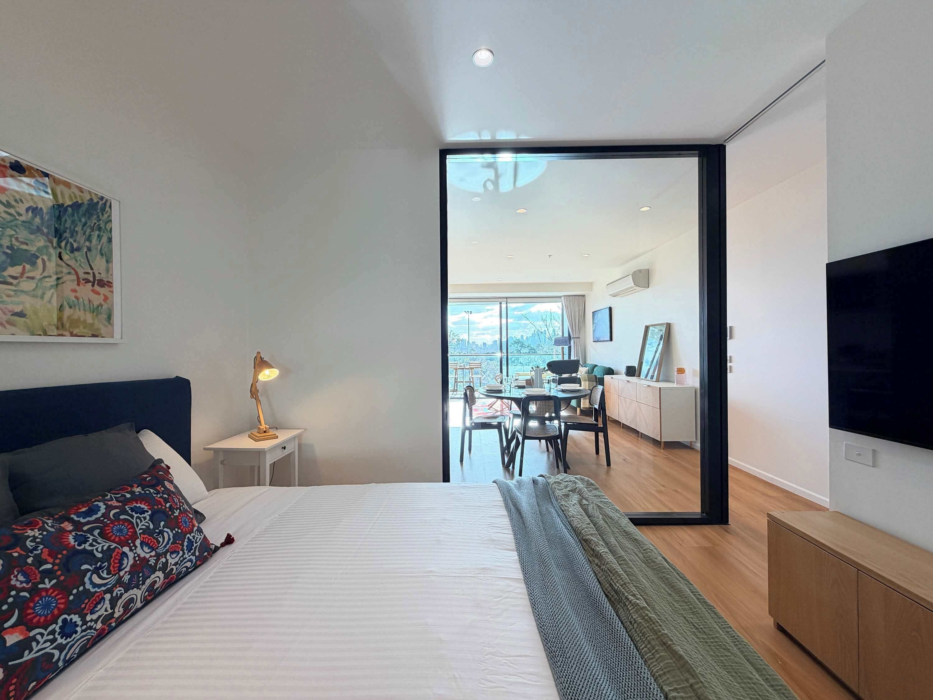 A modern bedroom with a bed, bedside lamp, and a large mirror.