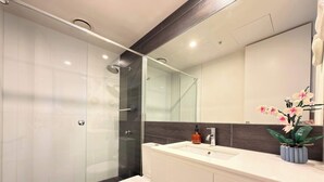 A modern bathroom with a glass-enclosed shower, a white toilet, and a vanity with a mirror. - St Kilda Retreat with Office + City & Park Views! (St Kilda)